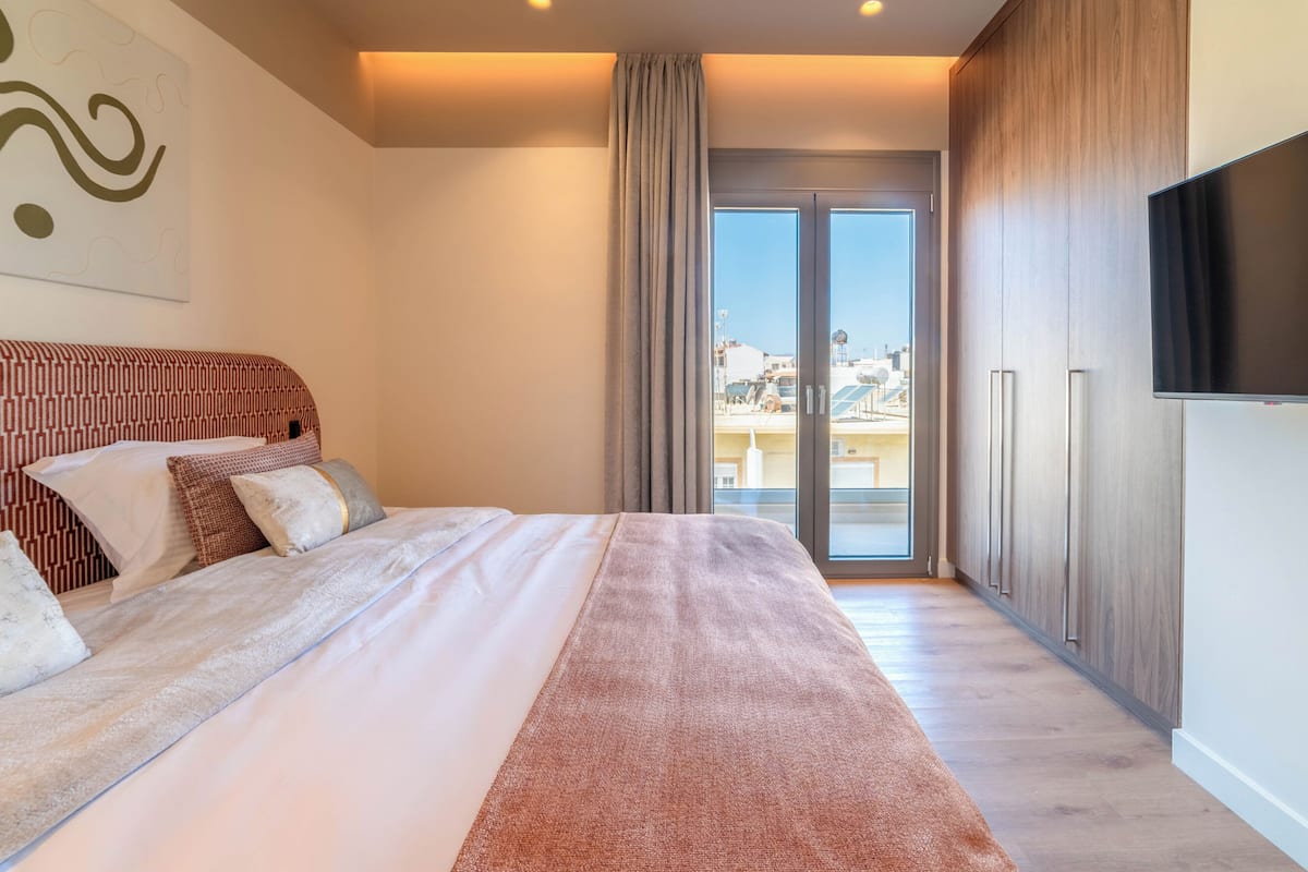 Habitación de hotel con cama, televisor, puerta corrediza de vidrio y vista de la ciudad.