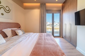 A hotel room with a bed, a TV, a sliding glass door, and a view of the city. - Minotaur's Rest (Heraklion)