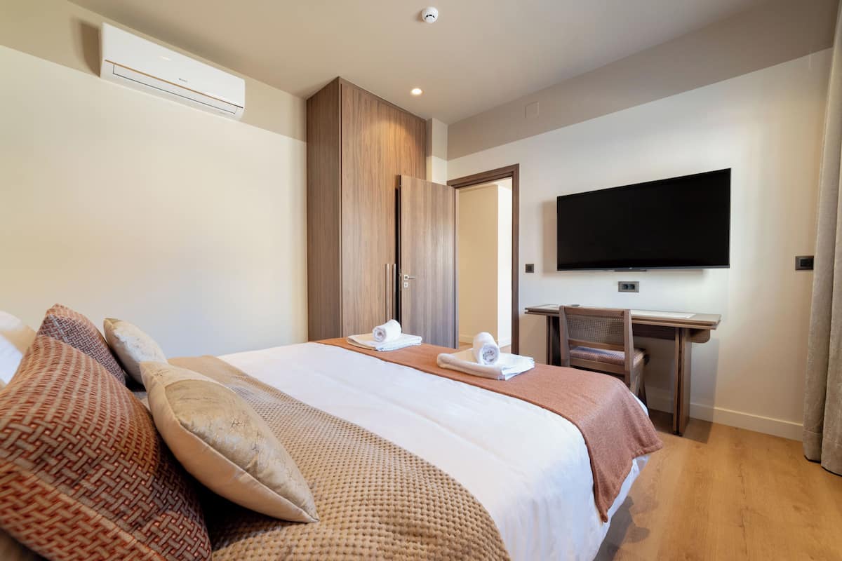 Una habitación de hotel con una cama, un escritorio, un televisor de pantalla plana y un armario.