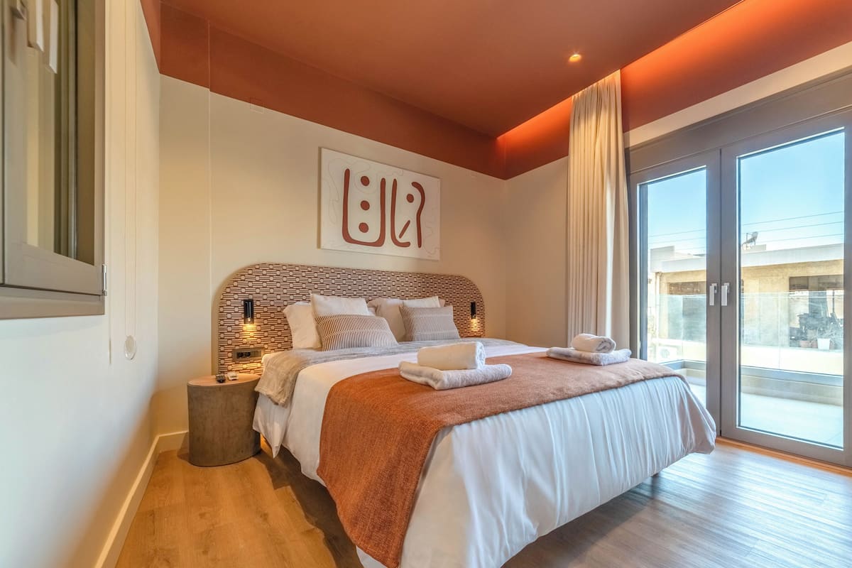 Un dormitorio moderno con una cama grande, un cabecero de diseño geométrico, una mesita de noche y vistas a través de una puerta corrediza de vidrio.