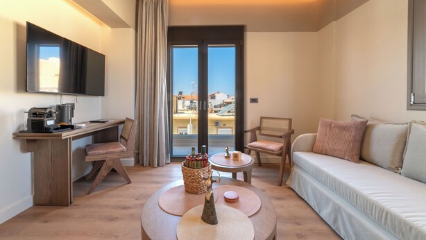 A modern living room with a sofa, a coffee table, a TV, a desk, and a view through a large window. - Minotaur's Rest (Heraklion)
