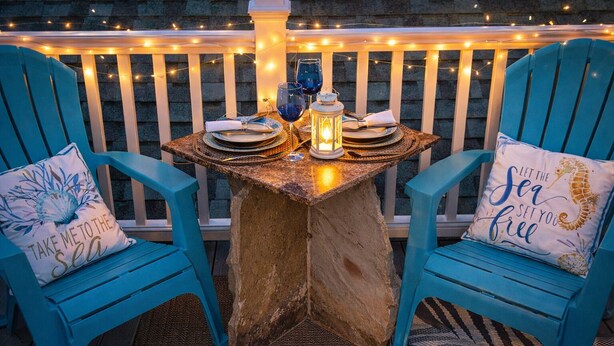 Un coin repas avec deux chaises bleues, une table dressée pour deux personnes et des guirlandes lumineuses.