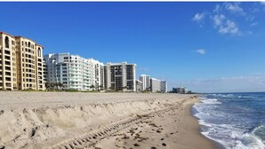 Uma praia com pegadas que levam a um complexo de hotéis altos.