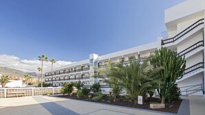 A modern hotel with multiple balconies, a landscaped courtyard with cacti and palm trees, and a clear view of the surrounding mountains. - Beachfront 1BR with Balcony, Pool & Parking Ancla (Callao Salvaje)