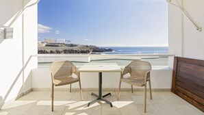 A balcony with two wicker chairs and a small table, overlooking a coastal view with buildings and the sea. - Beachfront 1BR with Balcony, Pool & Parking Ancla (Callao Salvaje)