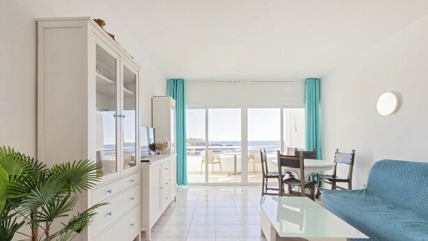 A modern living room with a sofa, a dining table, and a kitchen area with cabinets. - Beachfront 1BR with Balcony, Pool & Parking Ancla (Callao Salvaje)