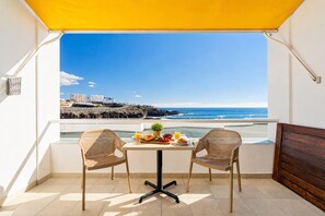 Un balcon avec deux fauteuils en osier, une petite table avec des éléments pour le petit-déjeuner et une vue sur la ville.