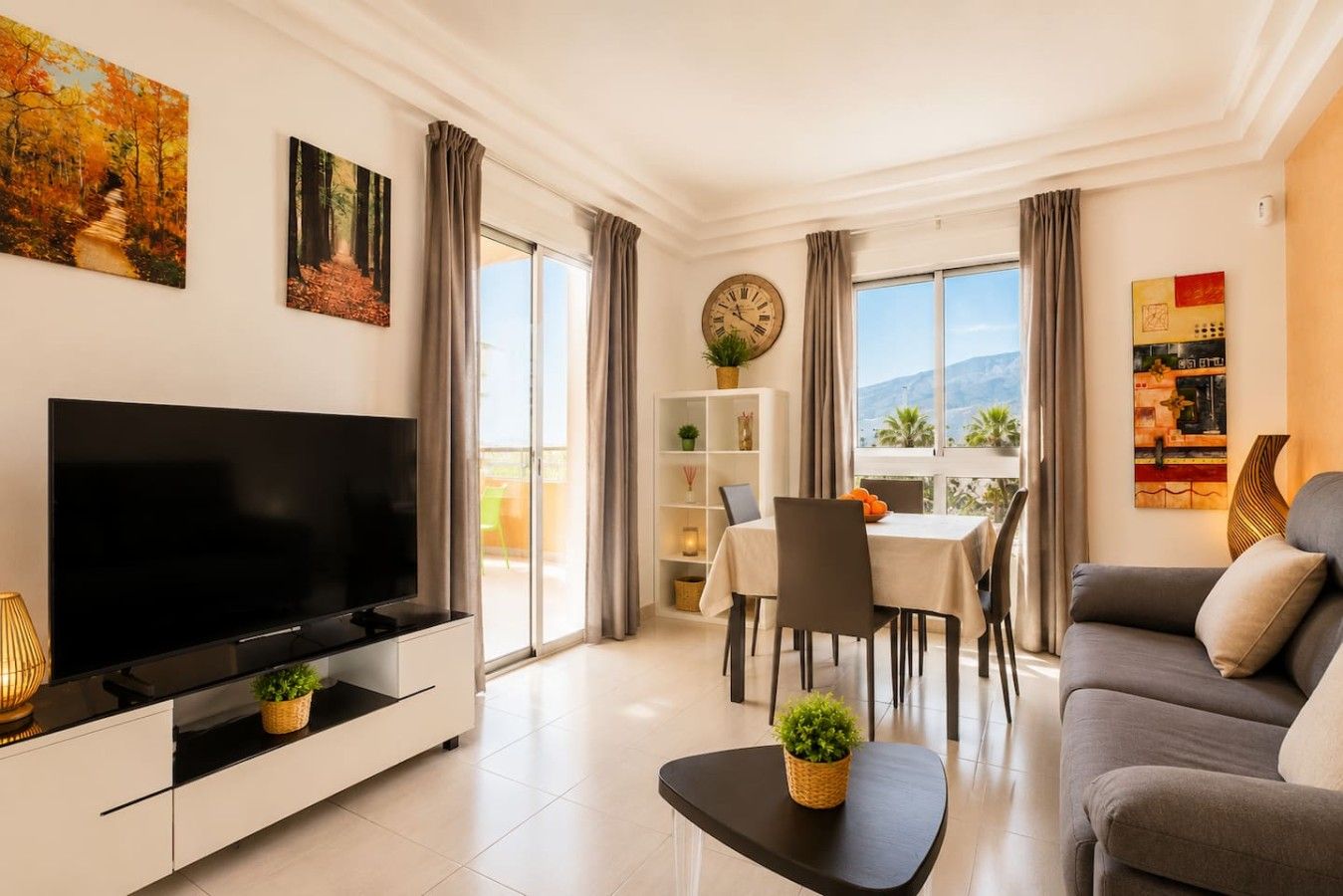 Ein modernes Wohnzimmer mit Flachbildfernseher, einer Couch, einem Esstisch mit Stühlen und einem Balkon mit Aussicht.