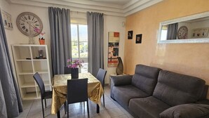 Ein Wohnzimmer mit Esstisch, grauem Sofa und einem großen Fenster mit Vorhängen.