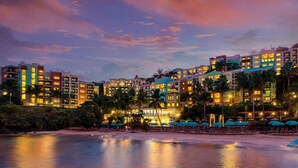 Un hotel sulla spiaggia con diversi edifici, palme e una spiaggia in primo piano.