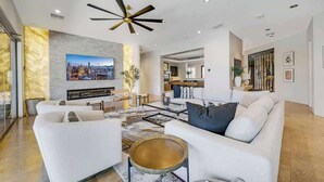 Ein großzügiger Wohnbereich mit modernem Deckenventilator, einem großen Flachbildfernseher, der an einer Marmorwand angebracht ist, und einer gemütlichen Sitzecke mit Sofa und Couchtisch.