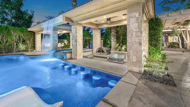 Ein Swimmingpool mit Whirlpool, einer Außendusche und einer Sitzecke, umgeben von Steinpfeilern und Grünpflanzen.