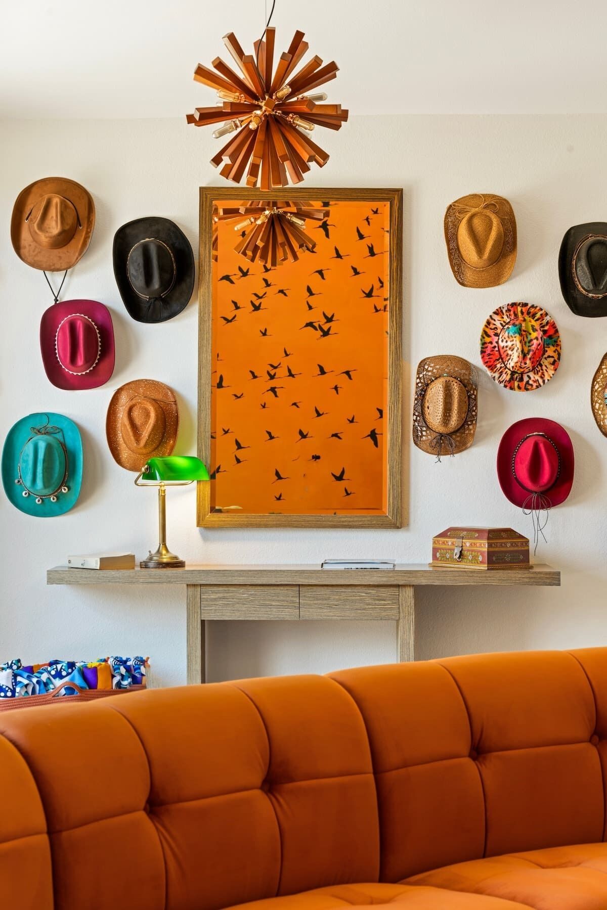 A room with a sofa, a table with a lamp, and a wall decorated with various hats.