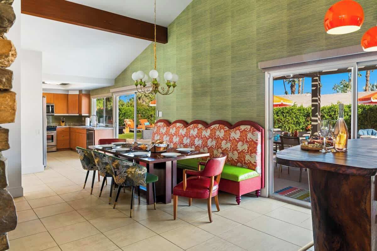 A dining area with a table set for four, surrounded by colorful chairs and a sofa with a floral pattern.