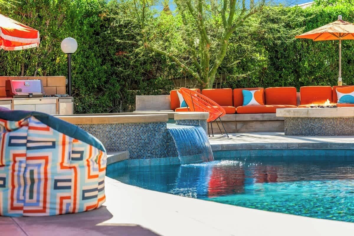 Un área de piscina con cascada, asientos exteriores y una parrilla.
