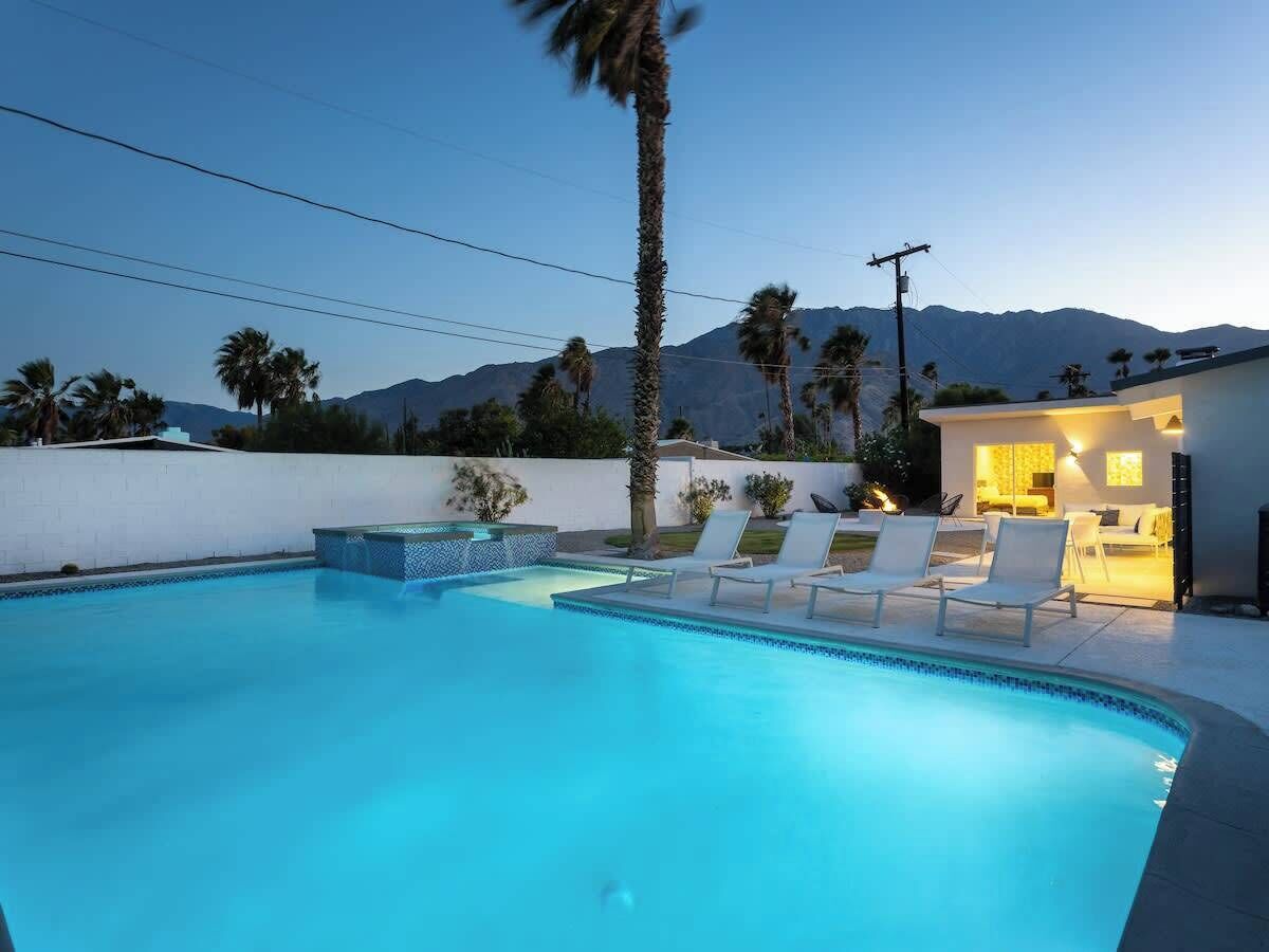 Una piscina con sillas de descanso, un pequeño jacuzzi y un edificio con iluminación cálida.