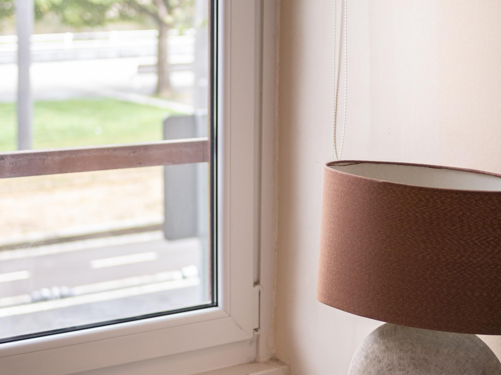A window with a view of a street and a lamp with a textured shade.