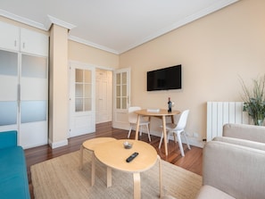 A modern living room with a dining area, a flat-screen TV mounted on the wall, and a sofa.
