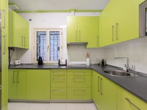 A kitchen with green cabinets, a window with floral curtains, a sink, and a kettle on the counter.