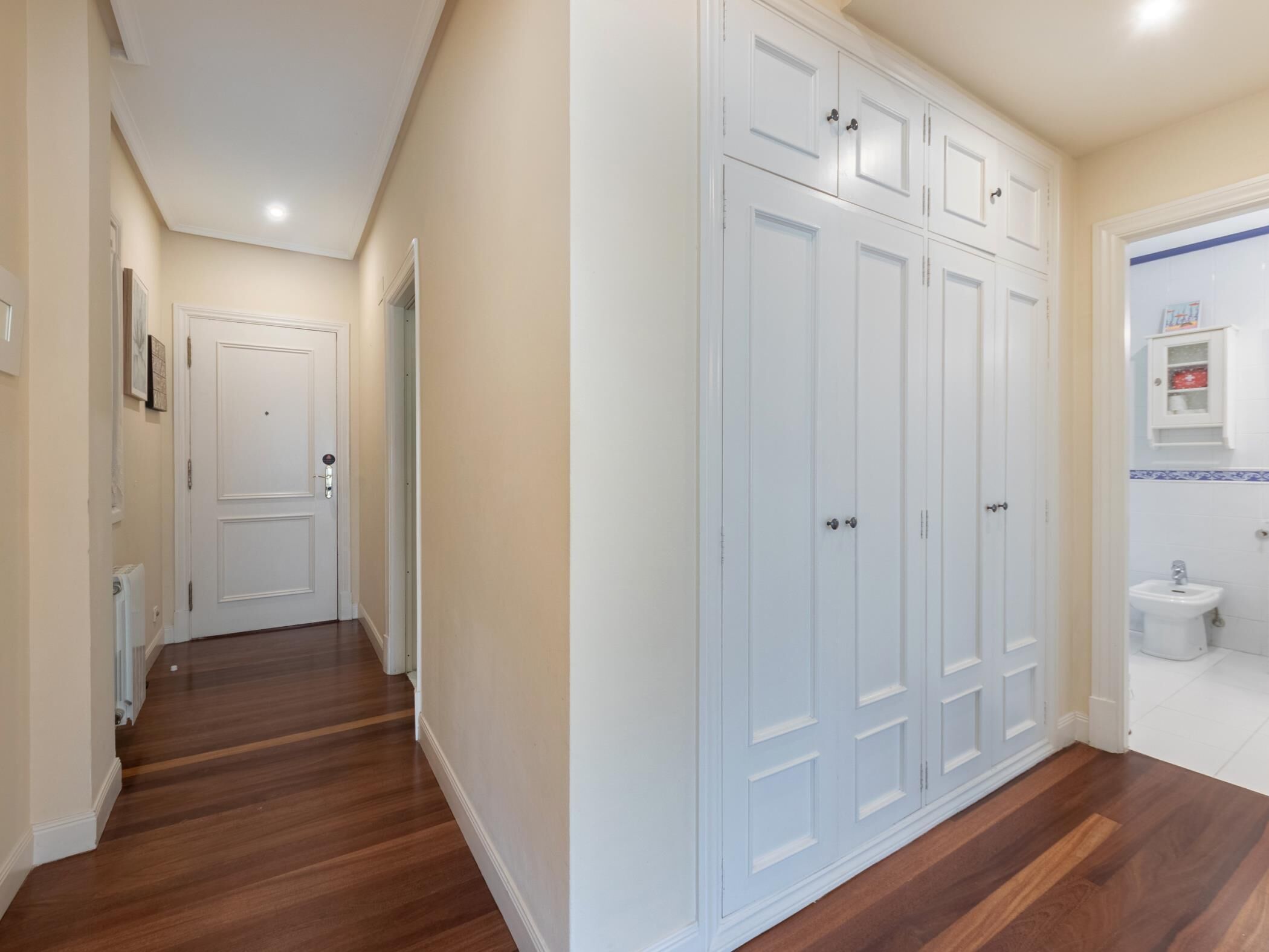 Un pasillo con suelo de madera, puertas blancas y un baño con inodoro y bidé.