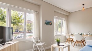 A modern living room with a TV, seating, a dining area, and large windows.