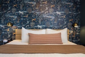 A bedroom with a large bed, two bedside lamps, and a wall with a nature-themed wallpaper. - The Arcade Oasis, fun for families in Loveland! (Loveland)