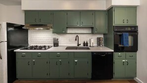Een keuken met groene kastjes, een zwarte kookplaat en een vaatwasser.