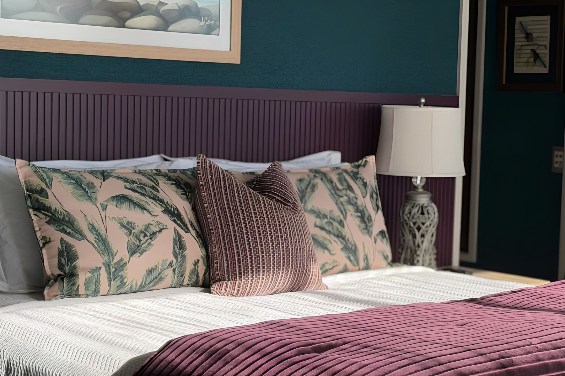 A bed with a patterned pillow, a bedside lamp, and a framed picture on the wall.