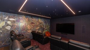 A home theater room with a large screen, reclining seats, and a mural of autumn leaves. - Tirohanga Nui (Oamaru)