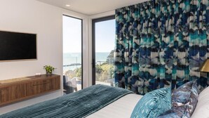 A modern bedroom with a large bed, a view of the sea, and a mounted TV. - Tirohanga Nui (Oamaru)