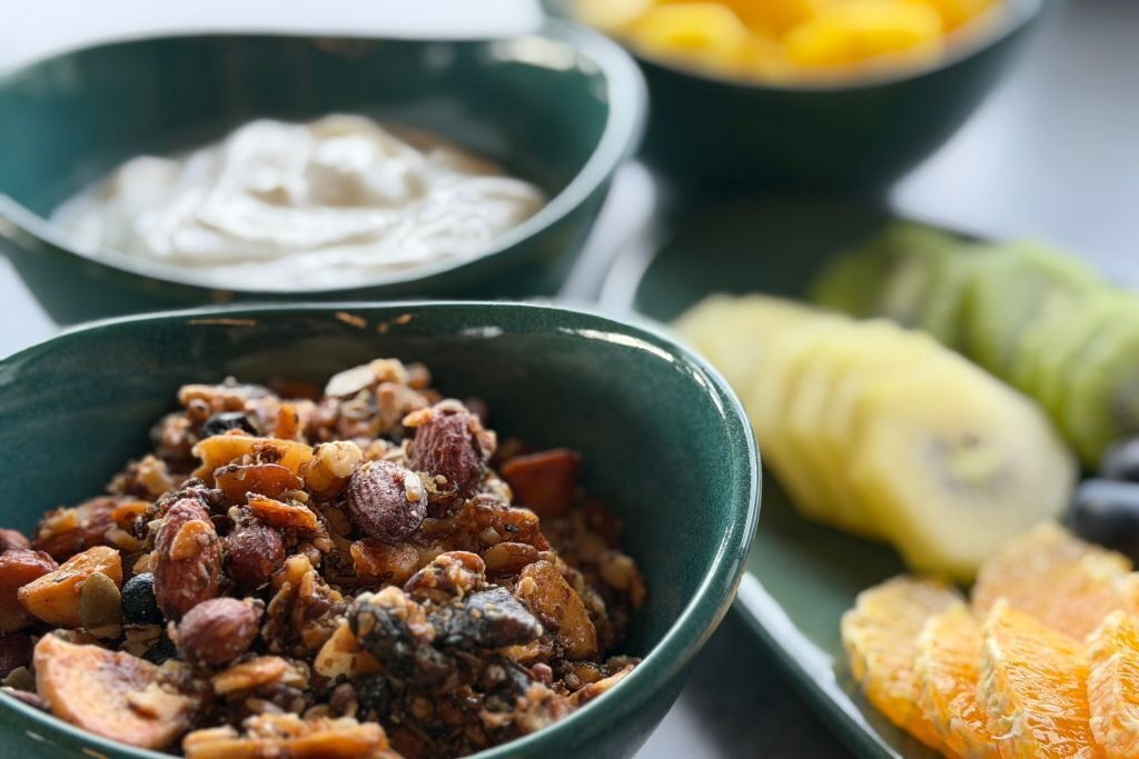 A bowl of mixed nuts and dried fruits, a bowl of yogurt, and a plate with sliced oranges and bananas.