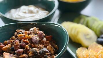 Un cuenco de frutos secos y frutas deshidratadas, un cuenco de yogur y un plato con rodajas de naranja y plátanos.