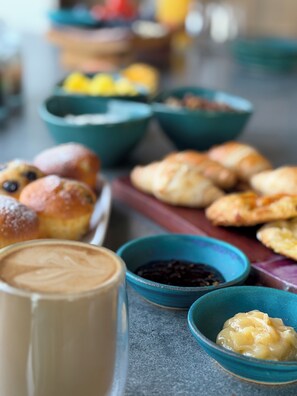 A table with various food items including pastries, bowls of condiments, and a glass of a brown beverage. - Tirohanga Nui (Oamaru)