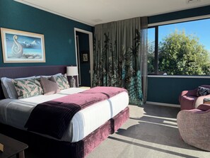 A bedroom with a bed, a nightstand, a chair, and a window with a view of trees. - Tirohanga Nui (Oamaru)