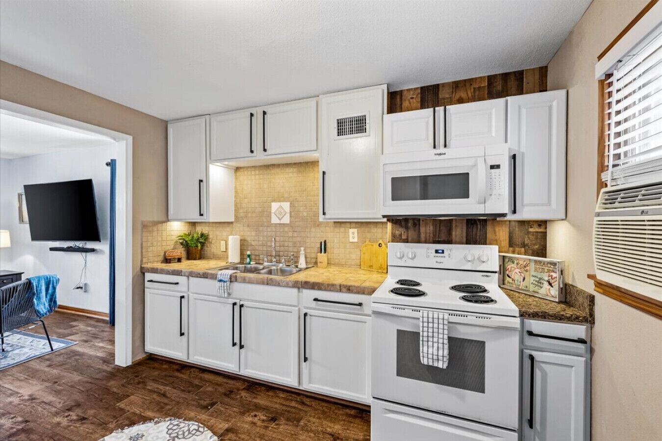 A modern kitchen with white cabinets, a microwave, stove, and a sink.