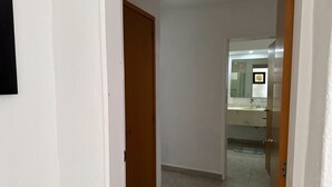 Een gang die leidt naar een badkamer met spiegel, wastafel en toilet.