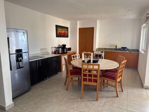 A compact kitchen with a refrigerator, a dining table with chairs, a microwave, and a coffee maker. - Awake to the Sea - Private beachfront apartment - Nuevo Vallarta (Bucerías)
