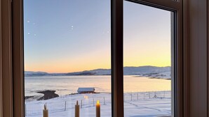 A window with a view of a snowy landscape and a body of water during sunset.