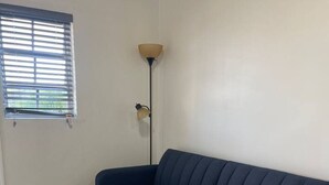 A room with a blue sofa, a small white table, a floor lamp, and a window with blinds. - Quiet 1BR: 4 mins to Beach 10 mins to Downtown (Nassau)