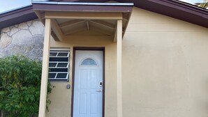 A house with a white door, a small porch, and a stone wall. - Quiet 1BR: 4 mins to Beach 10 mins to Downtown (Nassau)