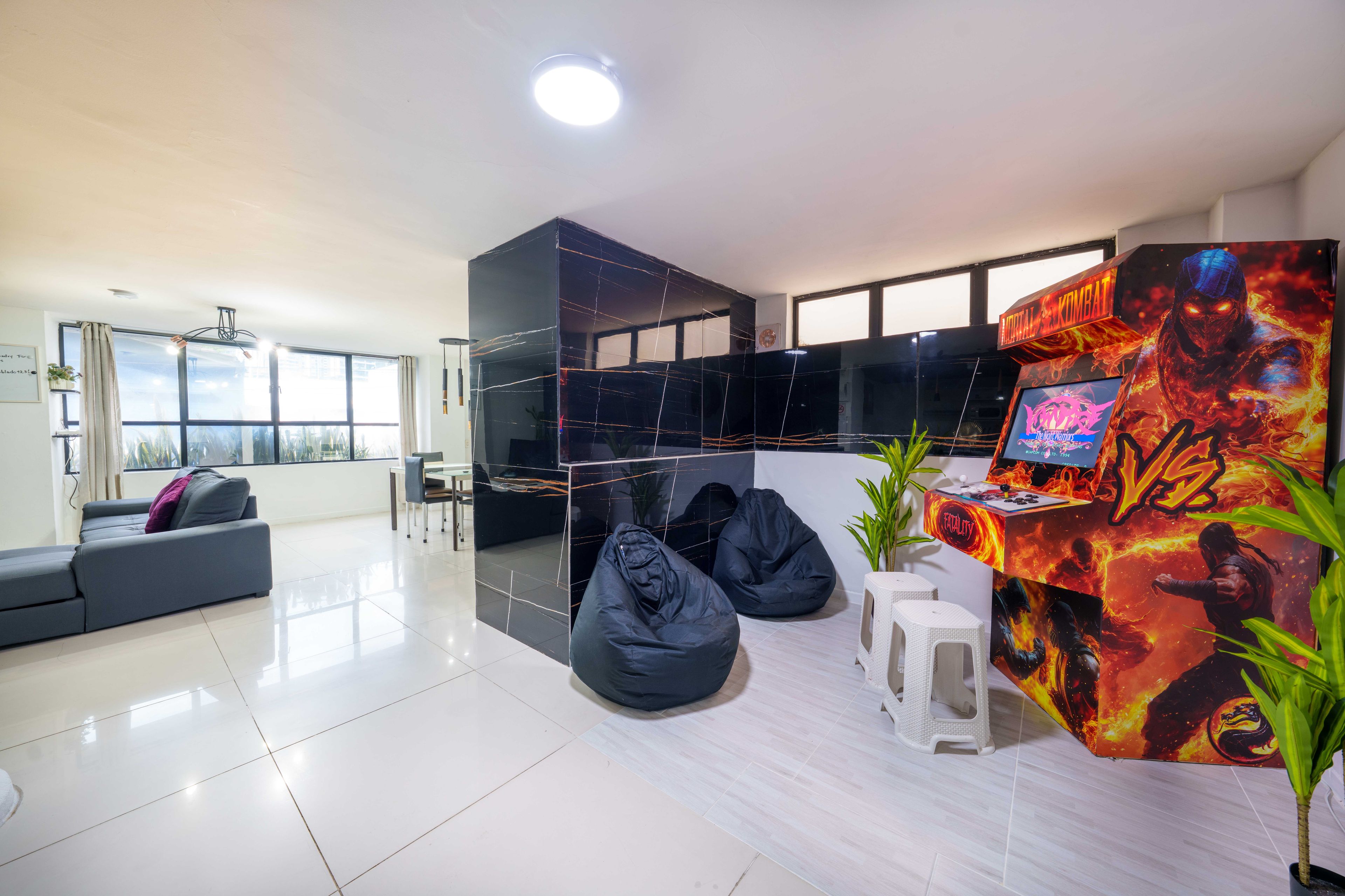 A modern living room with a black entertainment unit, a sofa, two bean bags, a small table, and a gaming console.