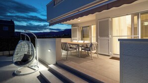 Eine moderne Außenpatio mit Esstisch und Stühlen, einem Hängesessel und einer Glasdoor, die zu einem überdachten Bereich führt.