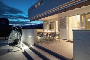 A modern outdoor patio with a dining table and chairs, a hanging chair, and a glass door leading to a covered area. - Family-Friendly 5-Bedroom Villa with Pool & Outdoor Space (Kaštel Kambelovac)