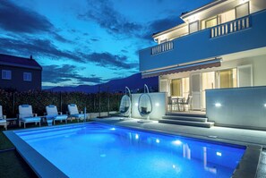 A modern two-story house with a swimming pool, outdoor seating, and a well-lit patio area. - Family-Friendly 5-Bedroom Villa with Pool & Outdoor Space (Kaštel Kambelovac)