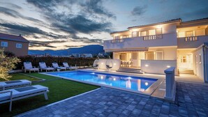 Ein modernes, zweistöckiges Haus mit Swimmingpool, Sitzgelegenheiten im Freien und Blick auf die Berge.