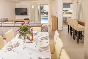 A dining area with a table set for four, a sofa, and a TV mounted on the wall. - Family-Friendly 5-Bedroom Villa with Pool & Outdoor Space (Kaštel Kambelovac)