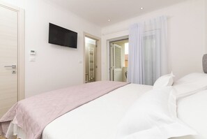 A bedroom with a bed, a television mounted on the wall, and a door leading to another room. - Family-Friendly 5-Bedroom Villa with Pool & Outdoor Space (Kaštel Kambelovac)