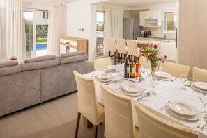 A dining area with a table set for four, a sofa, and a kitchen in the background. - Family-Friendly 5-Bedroom Villa with Pool & Outdoor Space (Kaštel Kambelovac)