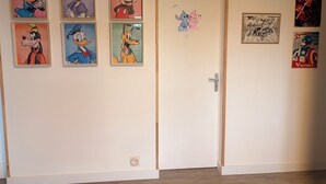 Una stanza con una porta bianca, sei poster incorniciati di personaggi Disney sul muro e un piccolo adesivo sulla porta.