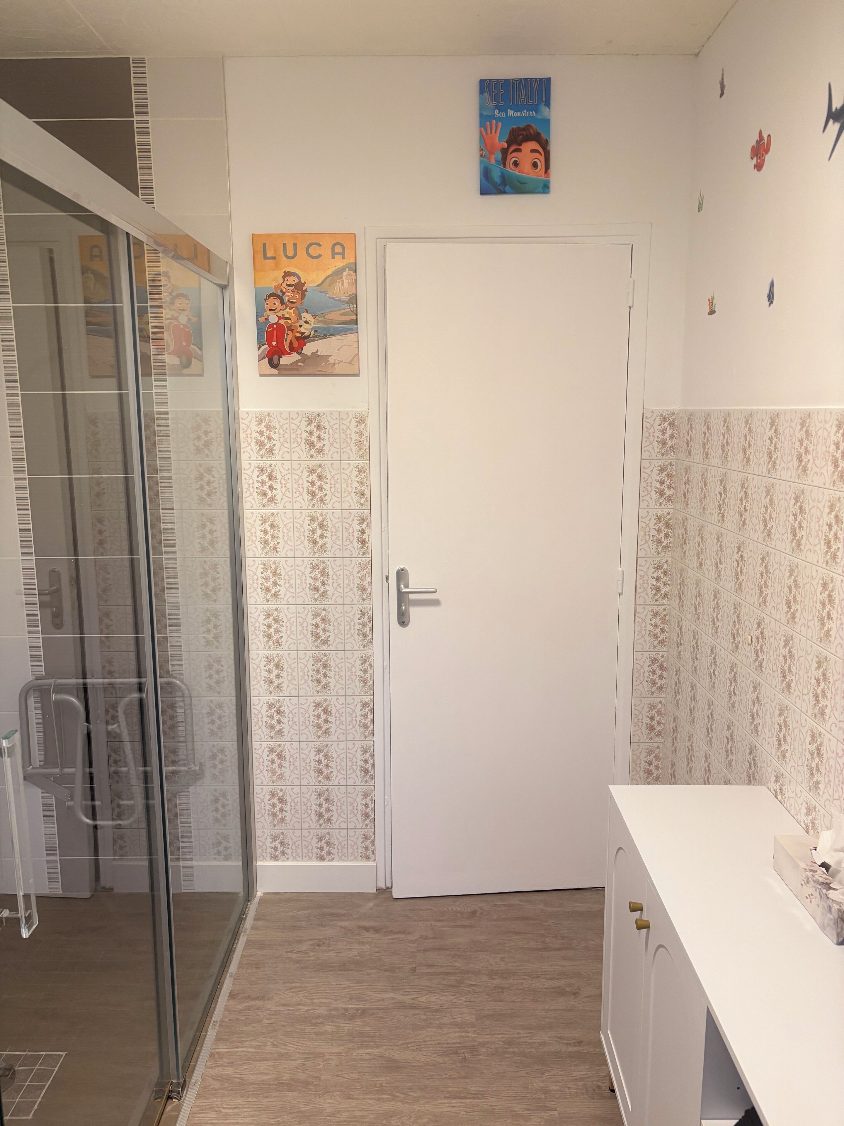 Un baño con baldosas estampadas, una puerta blanca y un cartel en la pared.